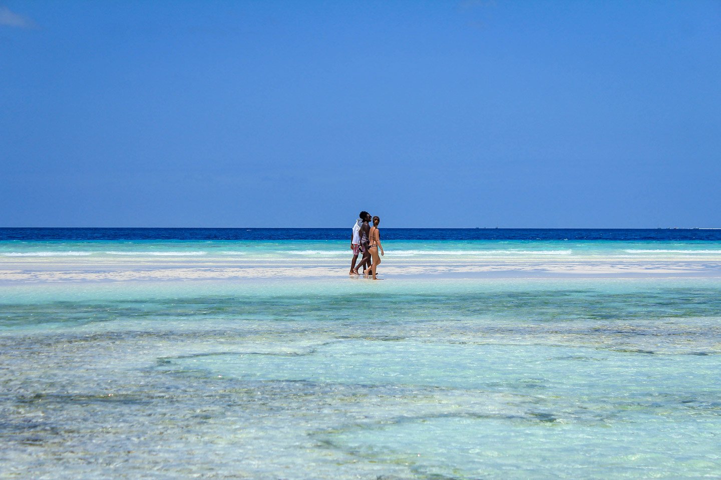 Carla, Malorie y Lando caminando en un banco de arena en Zanzibar.